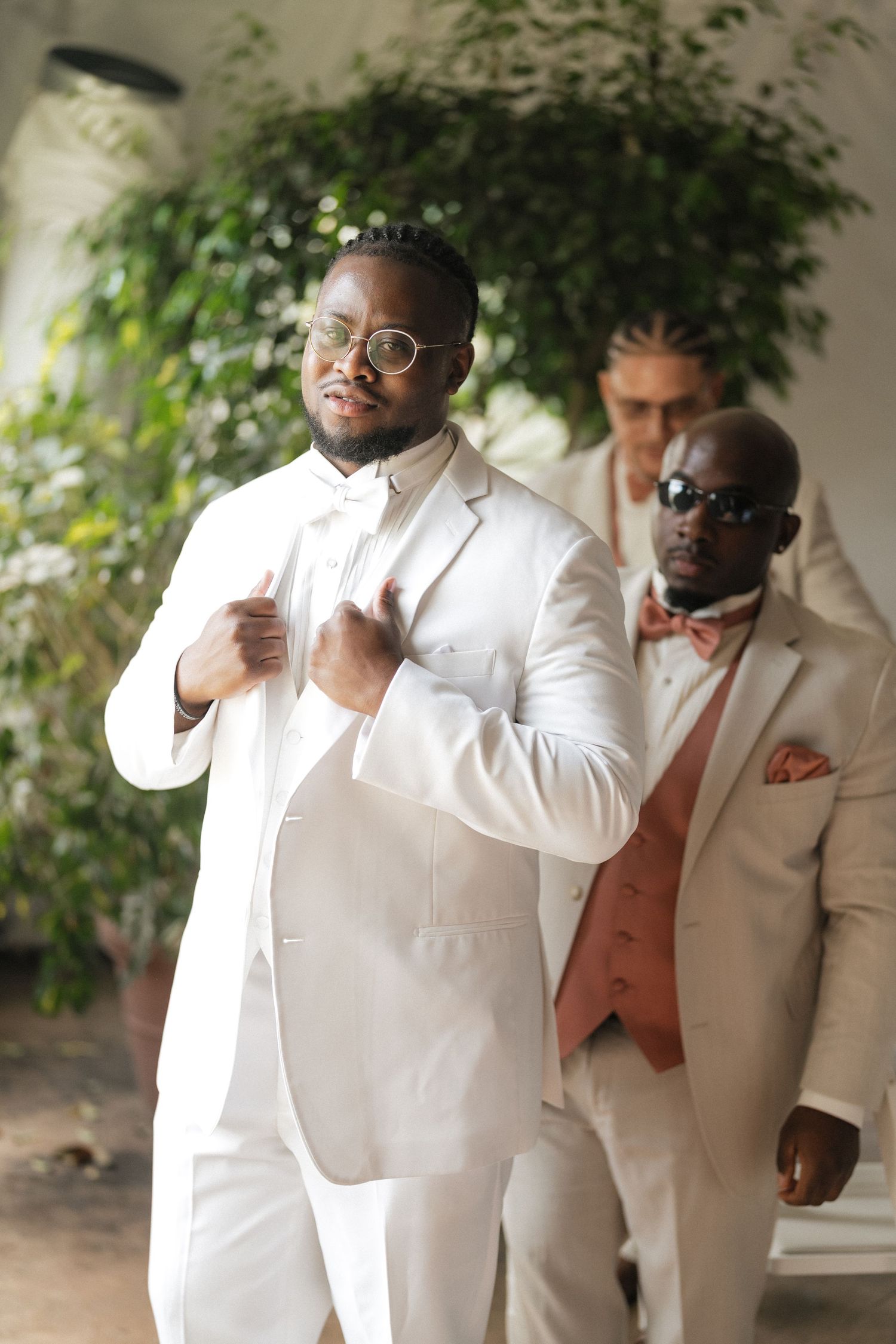 Wedding party members in white suits and coral vests strike playful poses in a series of candid shots.