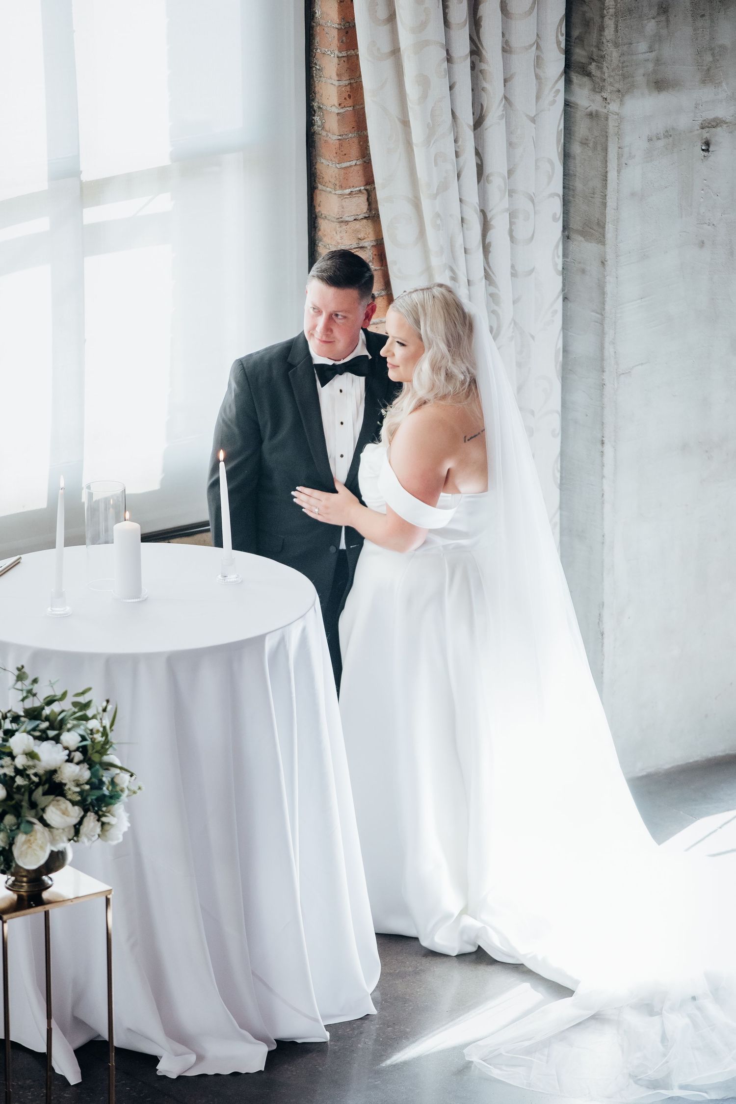 An elegant wedding couple shares intimate moments in a bright industrial space with white decor.