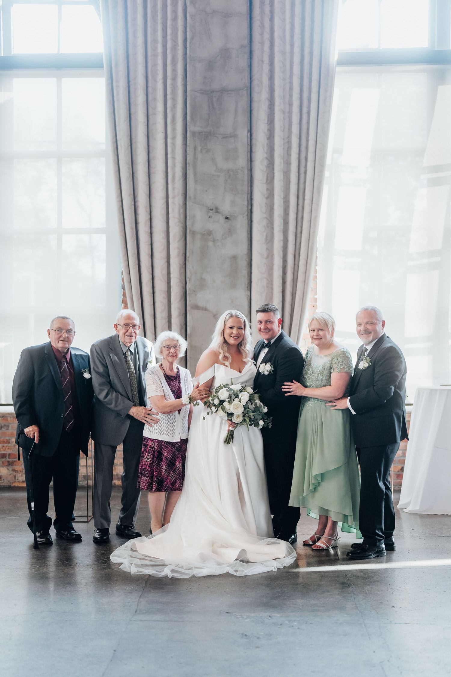 Wedding party poses together against a bright window in an elegant industrial space.