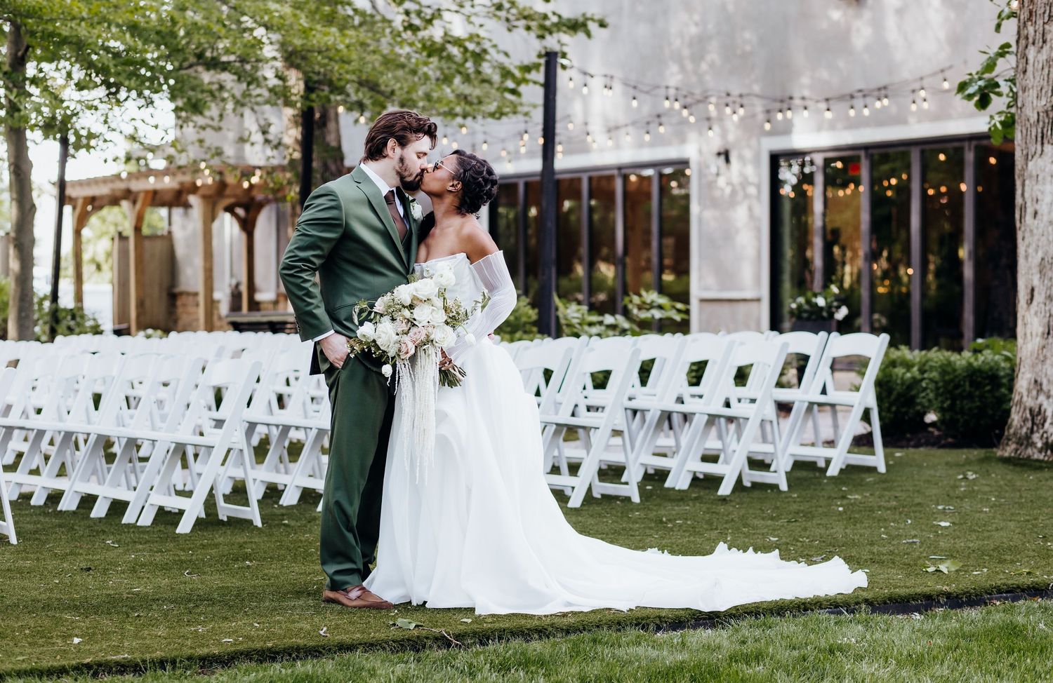 White ceremony chairs arranged on lawn with draped fabric decorations.
