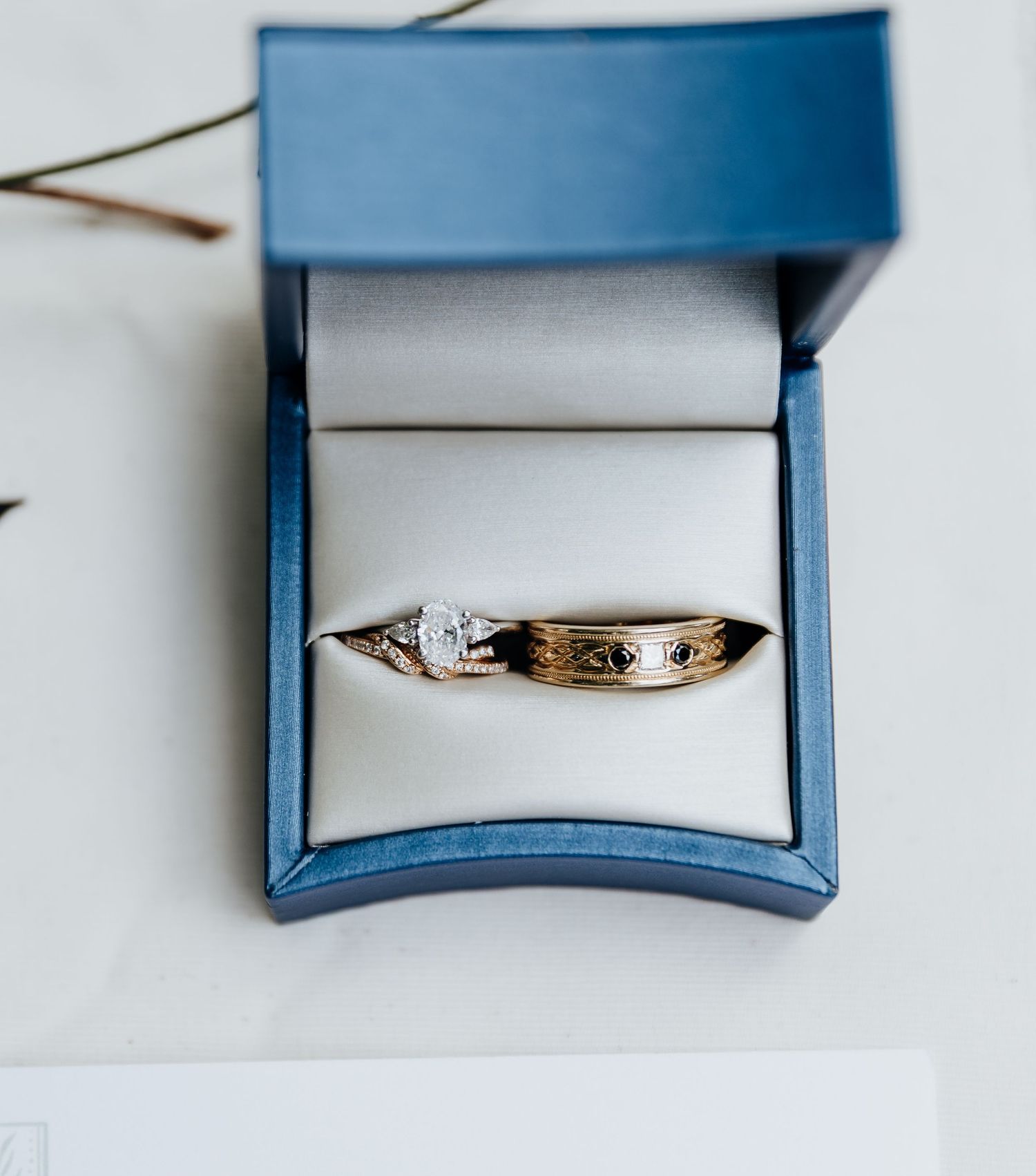 A silver wedding band with engraved details sits in a blue jewelry box on a white surface.