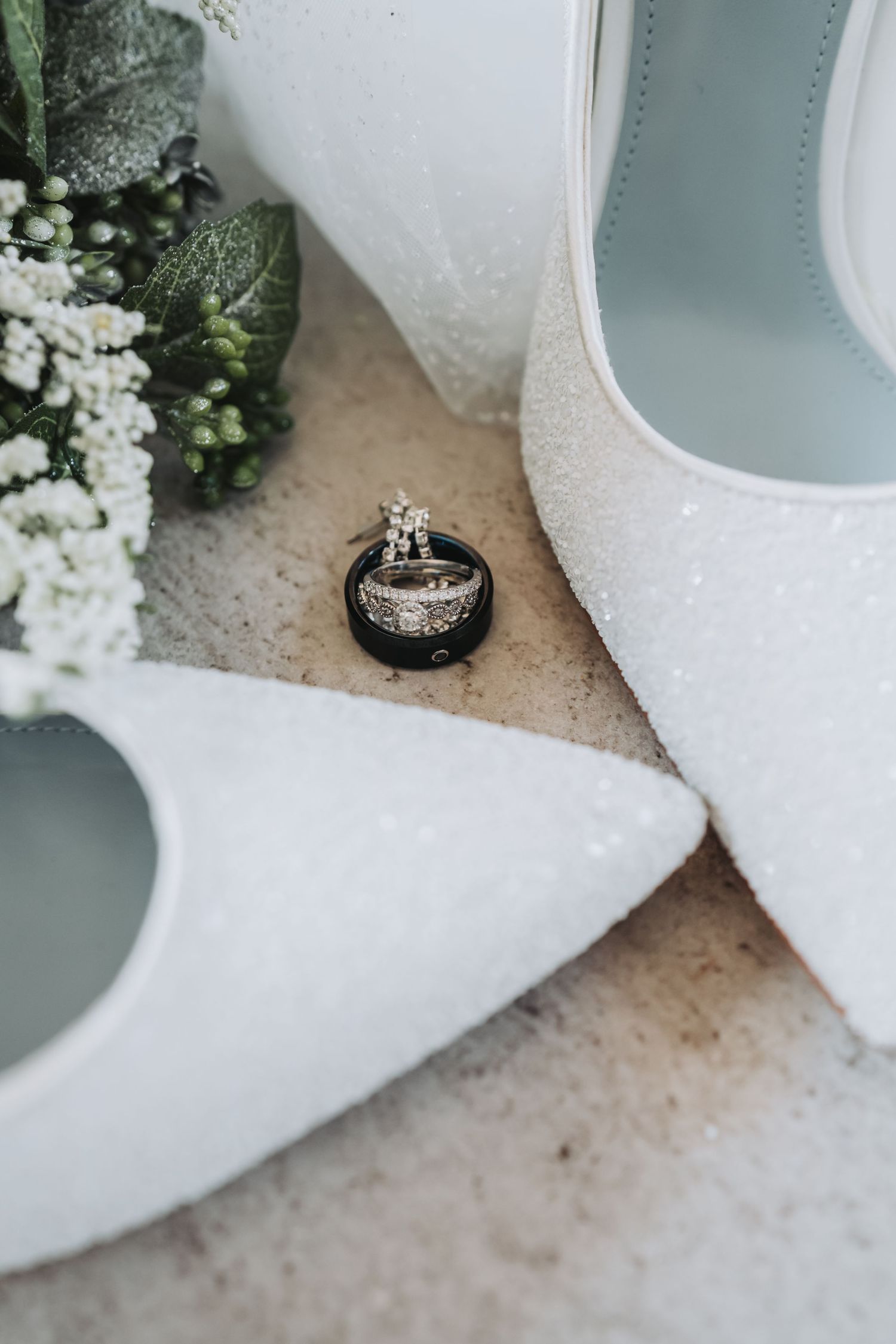 Wedding rings artistically placed beside white bridal shoes and delicate baby's breath flowers.