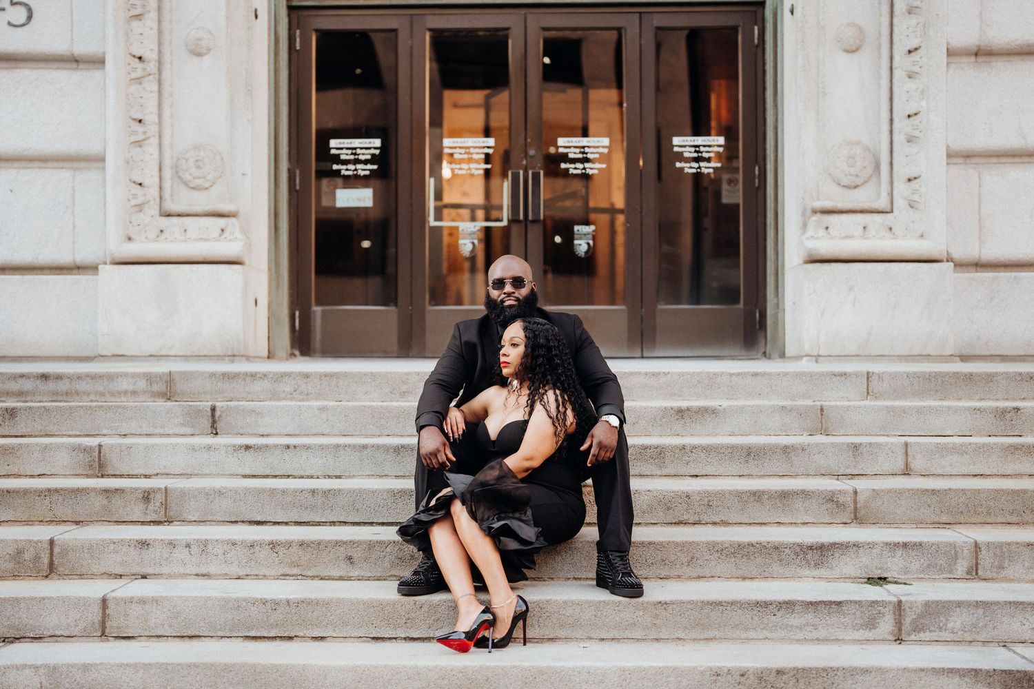 A couple shares a romantic moment on stone steps in front of ornate doors.