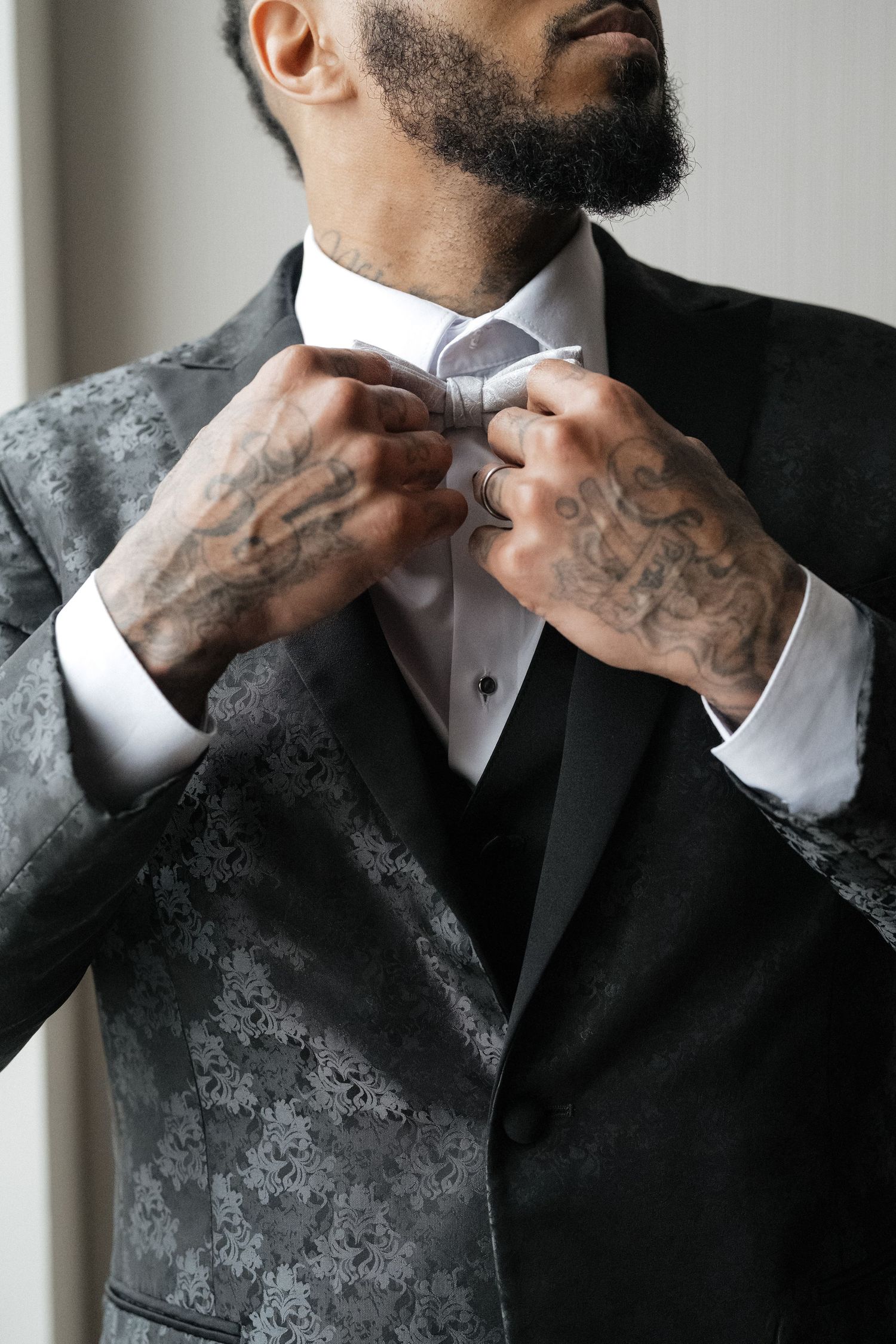 Close-up sequence showing hands adjusting a white bowtie against a black suit with a textured grey pattern.