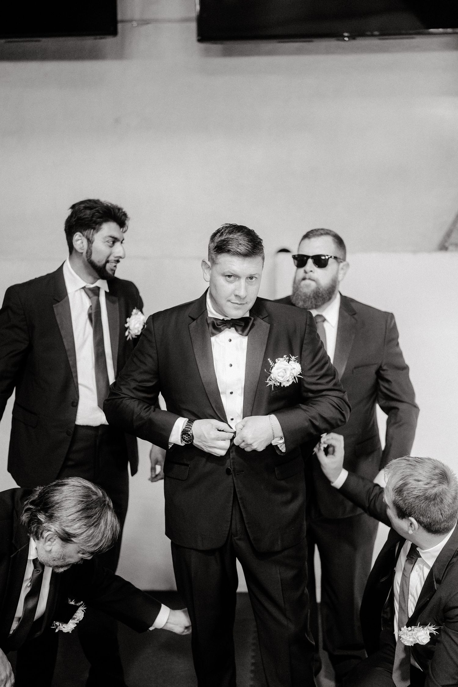 Groomsmen in black tuxedos sharing a candid moment before the wedding ceremony.