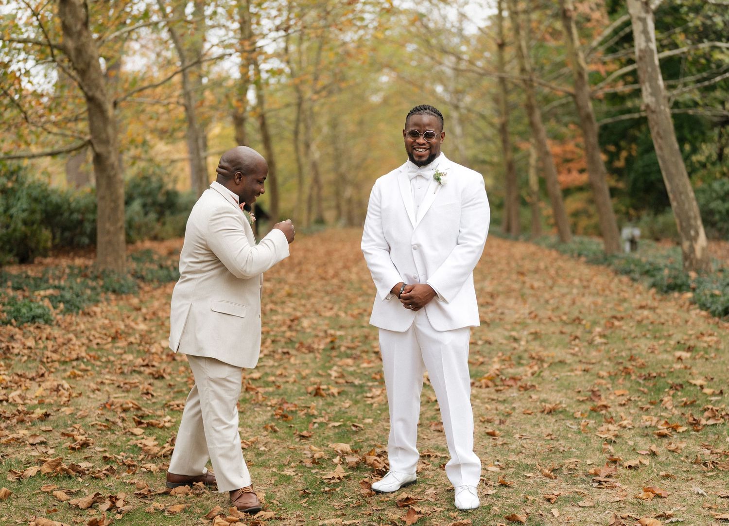 Wedding couple in matching white attire pose on leaf-covered ground.
