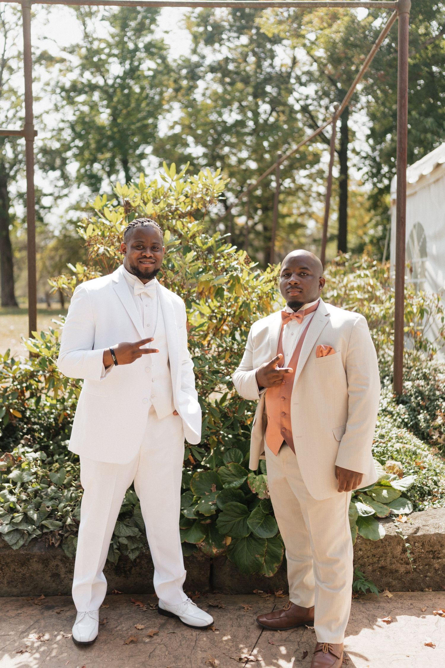Wedding party members in white suits share candid moments in an outdoor garden.