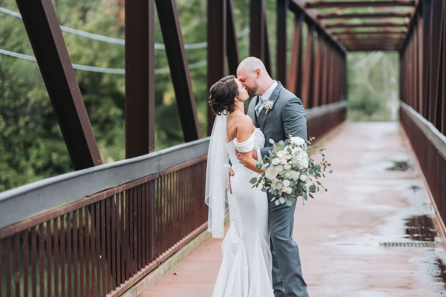 Romantic wedding moment captured on a rustic wooden bridge surrounded by greenery.