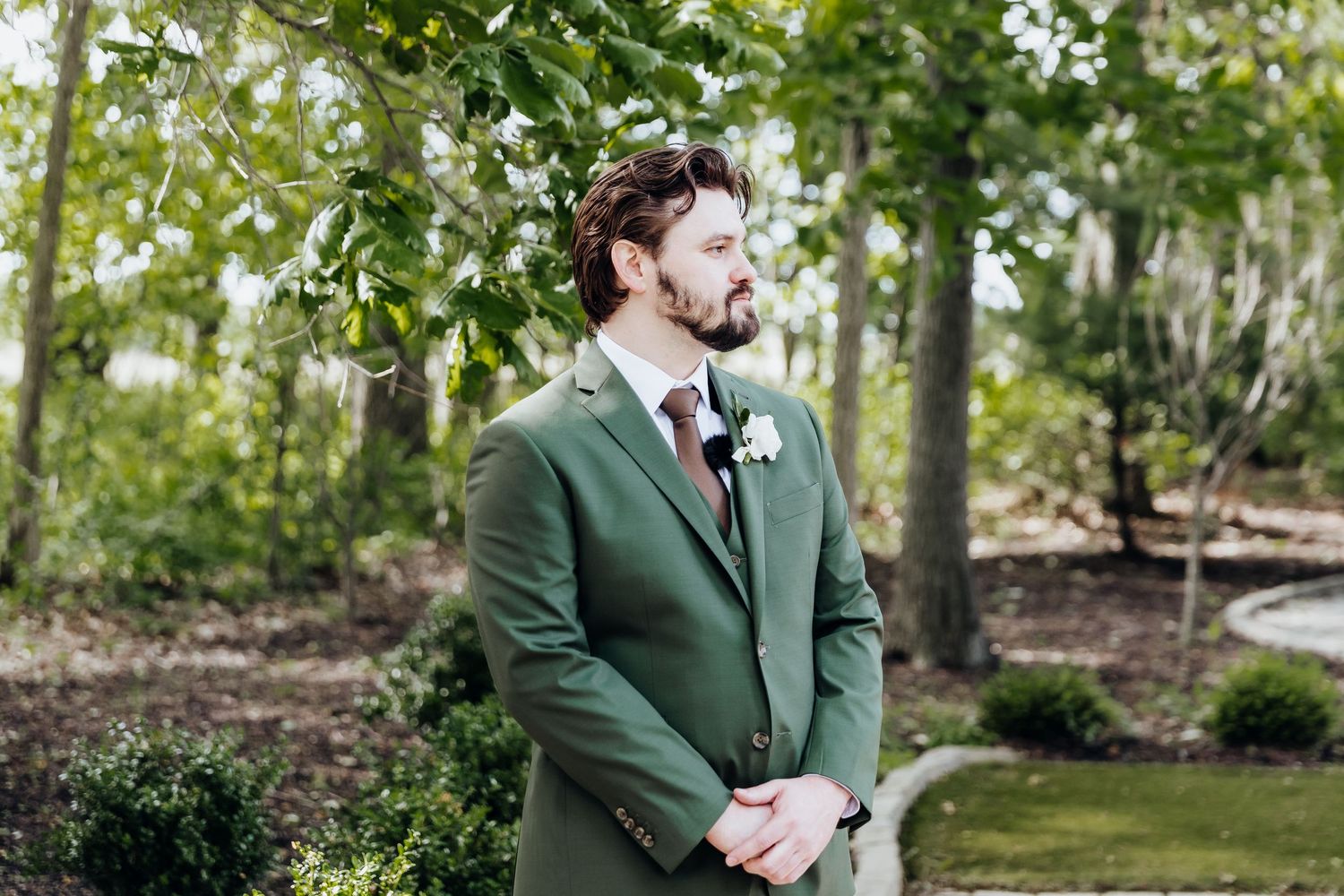 Outdoor wedding ceremony setup with green foliage and white chairs under natural light.