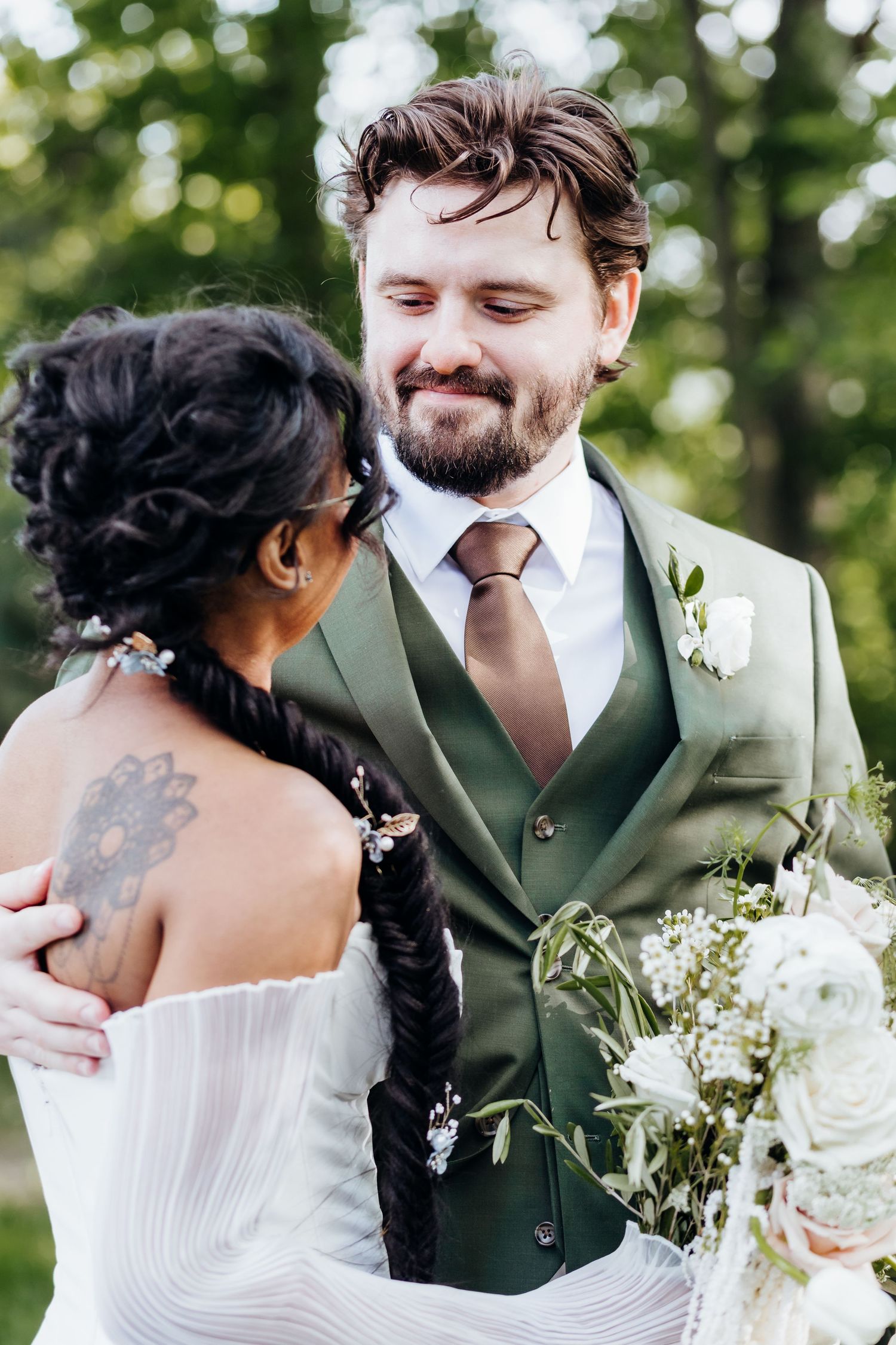Intimate wedding portraits showing couple in green suit and white dress against natural backdrop.