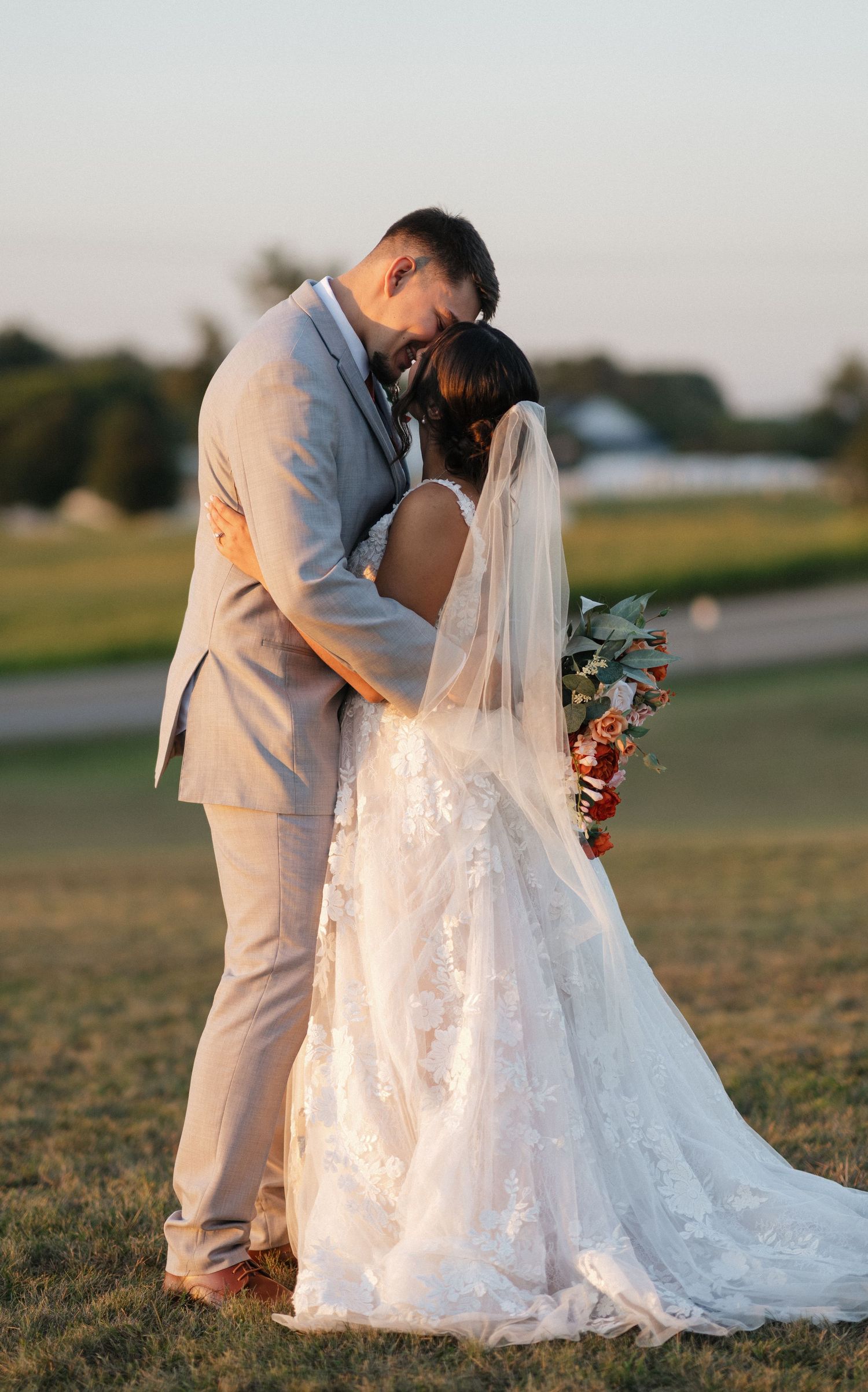 Romantic sunset wedding photos showing tender moments between newlyweds in a grassy field.