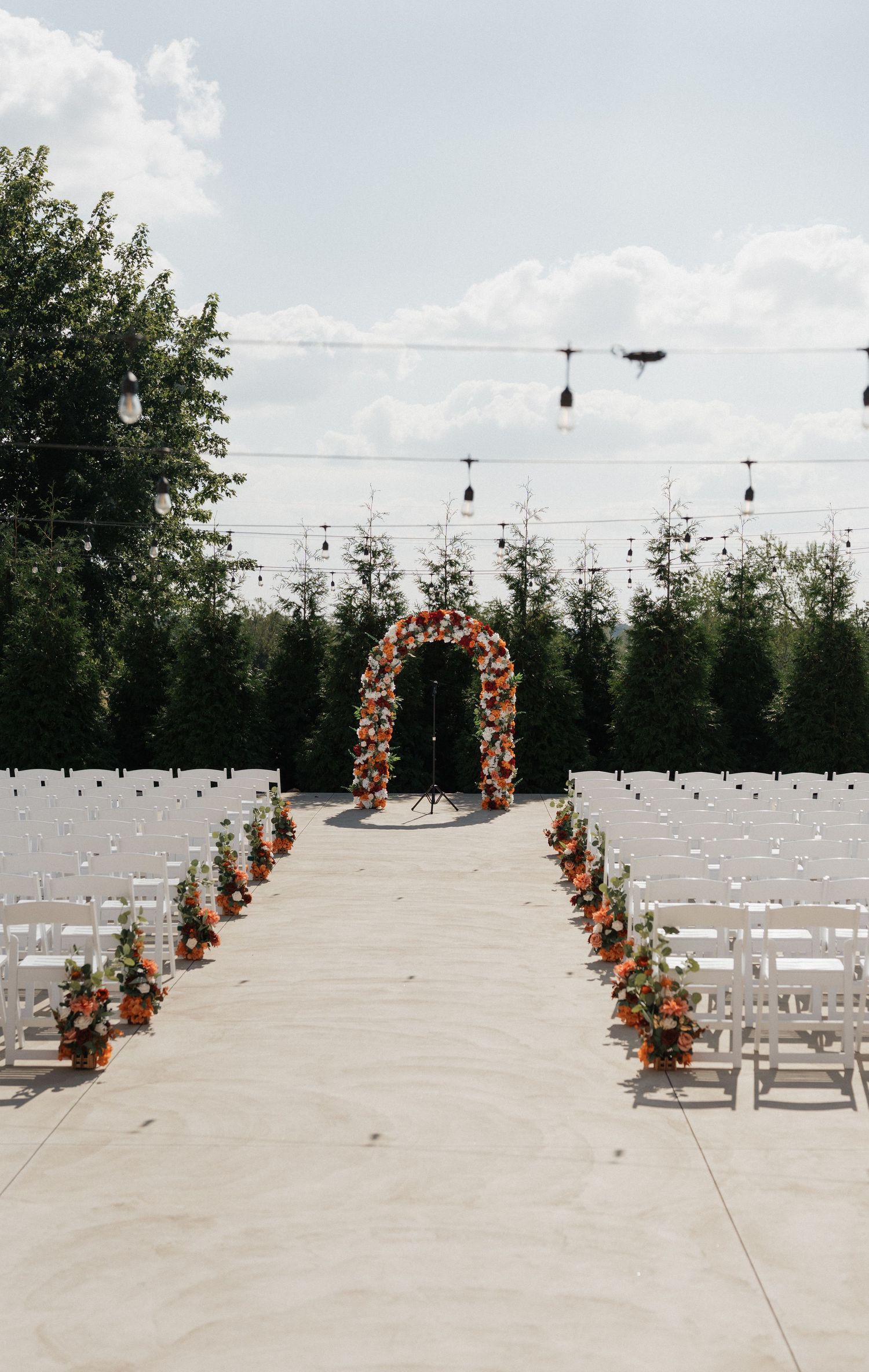 Outdoor wedding ceremony setup with white chairs and orange floral arch decorations.