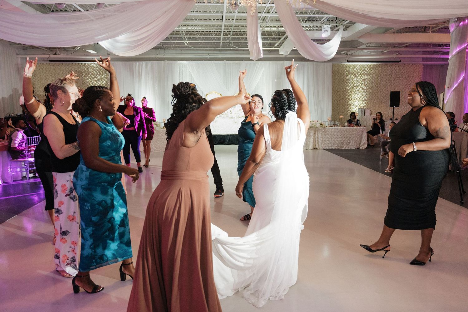 Wedding reception with pink draping and purple lighting shows guests dancing.