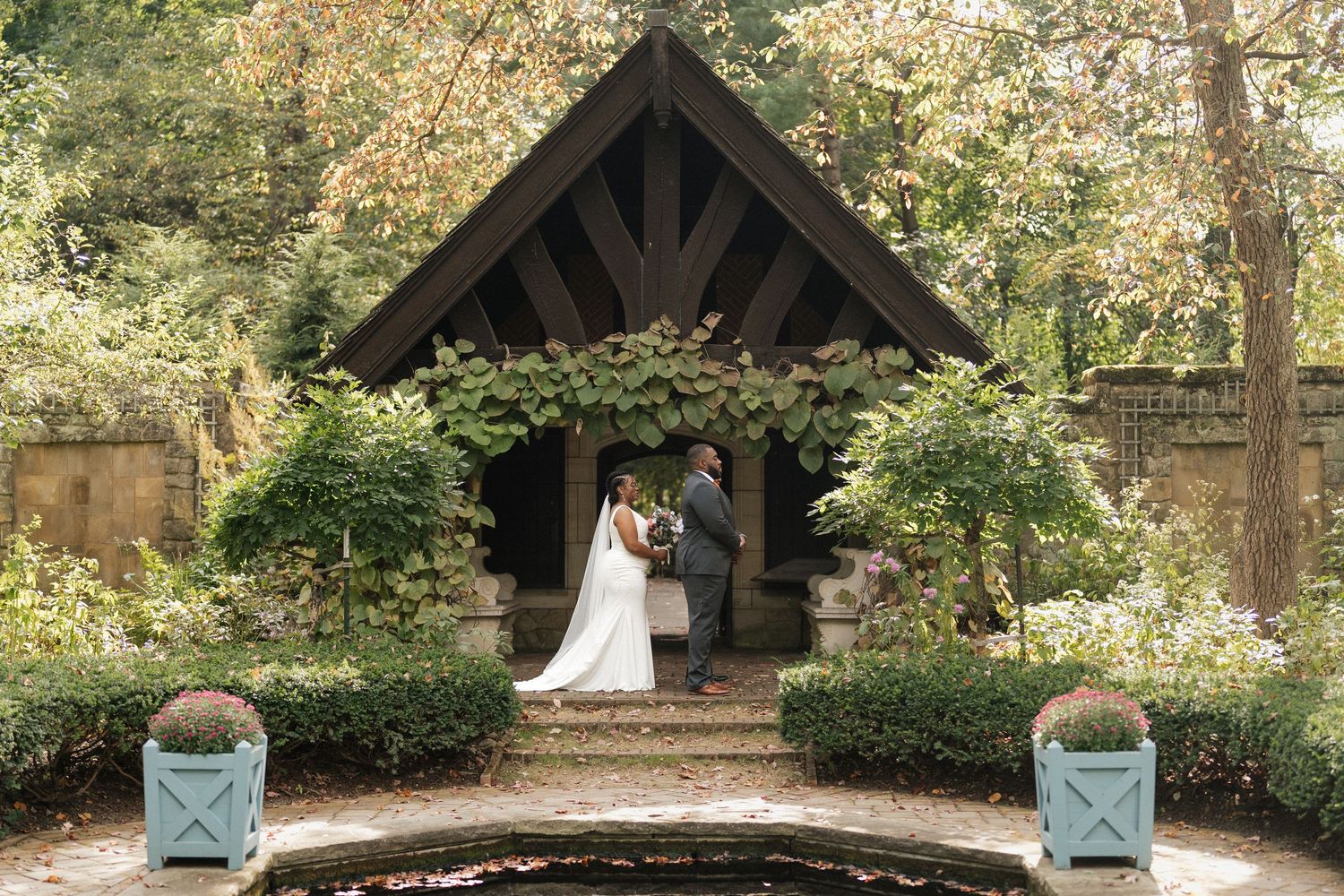 Outdoor wedding ceremony setup with wooden pavilion and chairs arranged in garden setting.