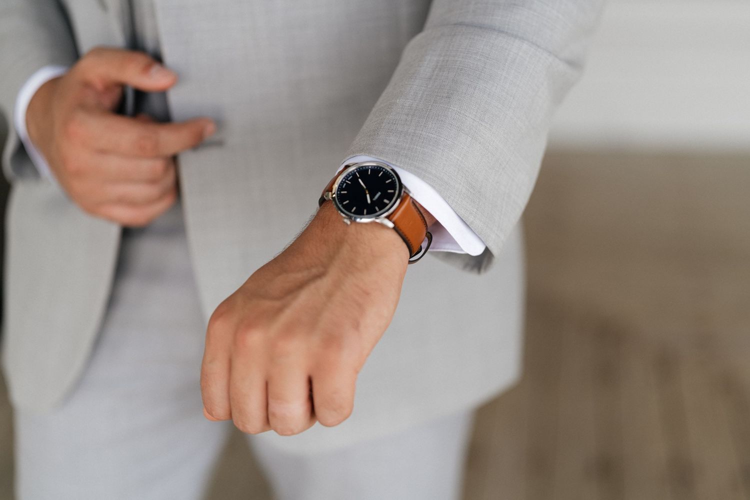 Close-up detail of brown leather dress shoes worn with light gray suit pants.