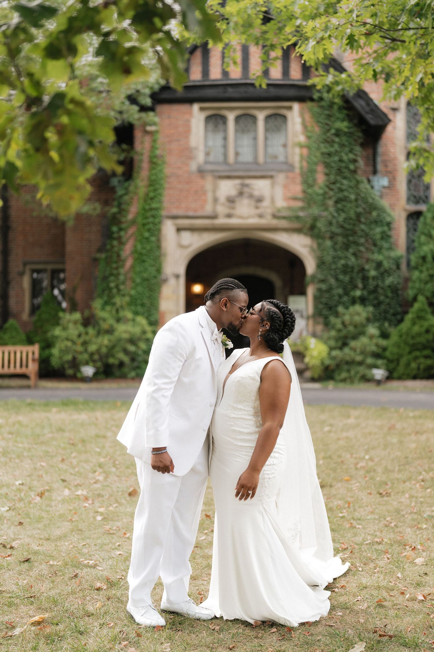 Newlyweds share intimate moments on the lawn of a historic brick building during autumn.