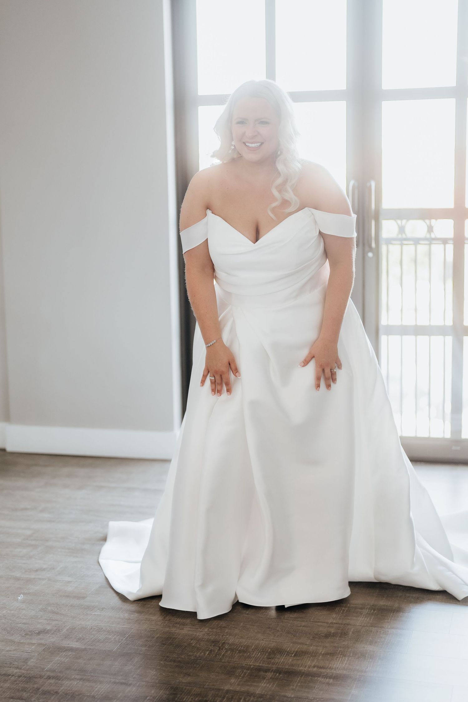 Close-up details of a white wedding gown against a light wooden floor.