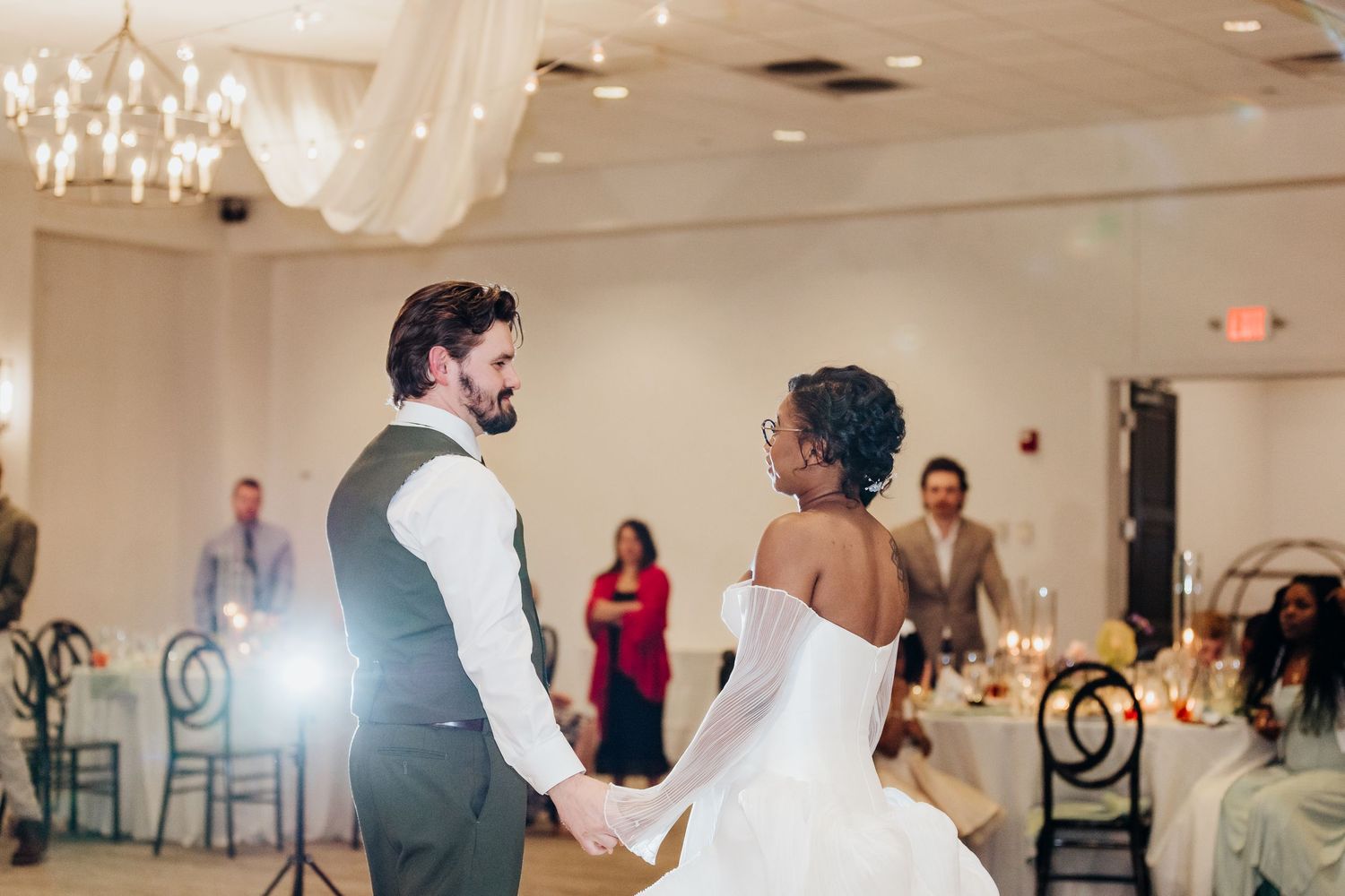 Couple sharing their first dance in an elegant ballroom with chandelier lighting.