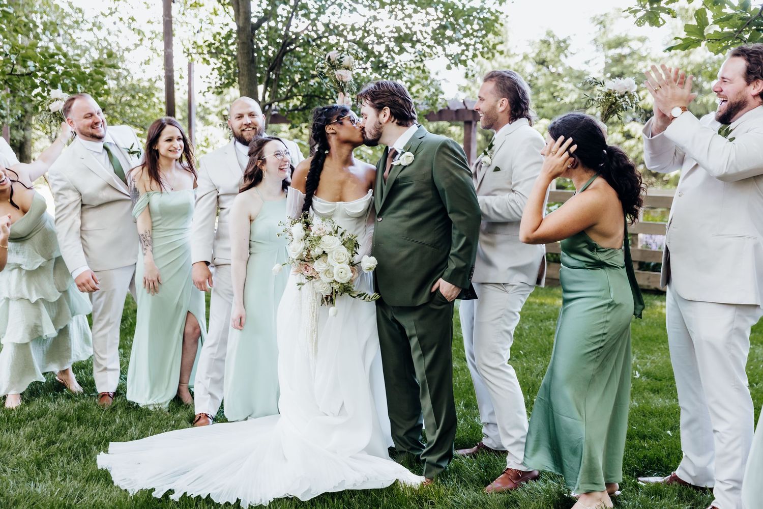 Large wedding party in mint and white attire celebrates outdoors under trees.