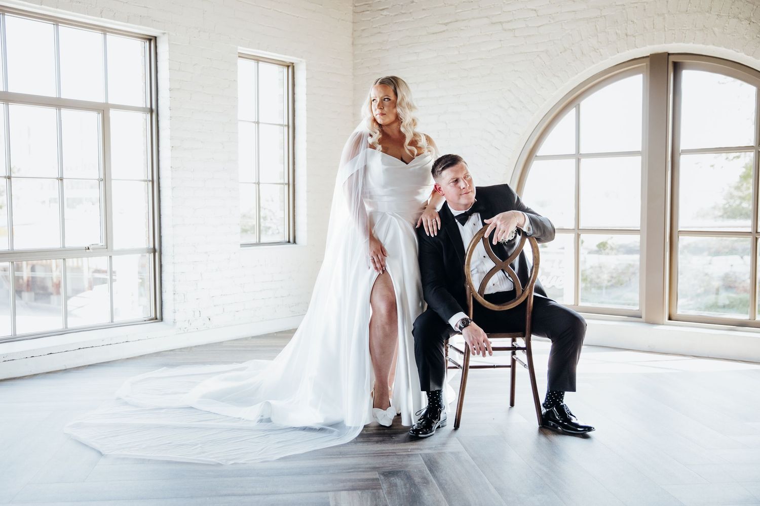 Wedding party members in formal attire pose in an elegant white room with large windows.