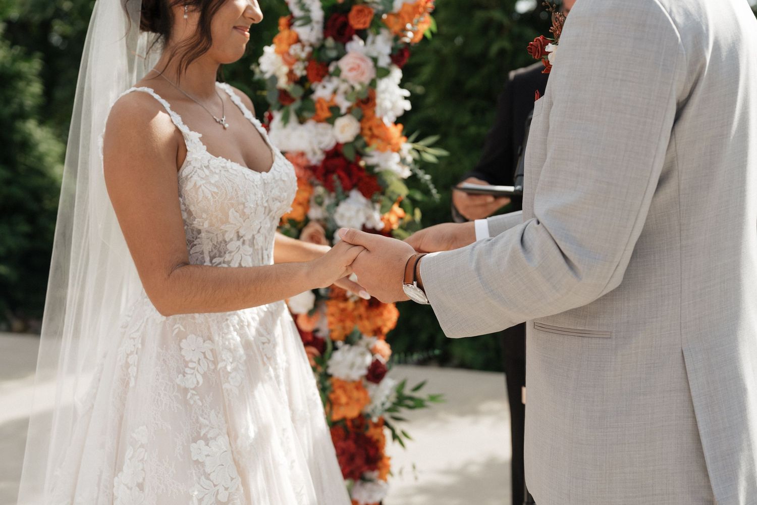 Close-up of couple exchanging rings during wedding ceremony with orange floral decor.