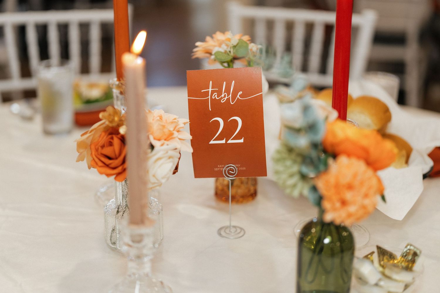 Wedding reception table with orange floral centerpieces and brown table numbers.