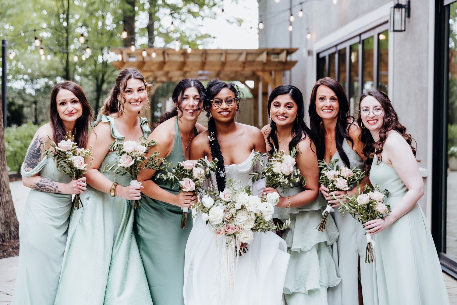 Bridesmaids in mint green dresses pose together holding floral bouquets outdoors.
