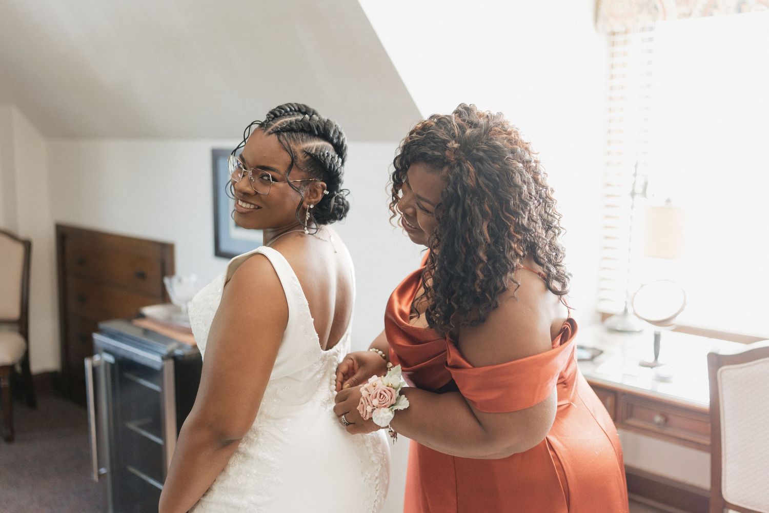 Two people in formal attire prepare for a wedding celebration in a sunlit room.