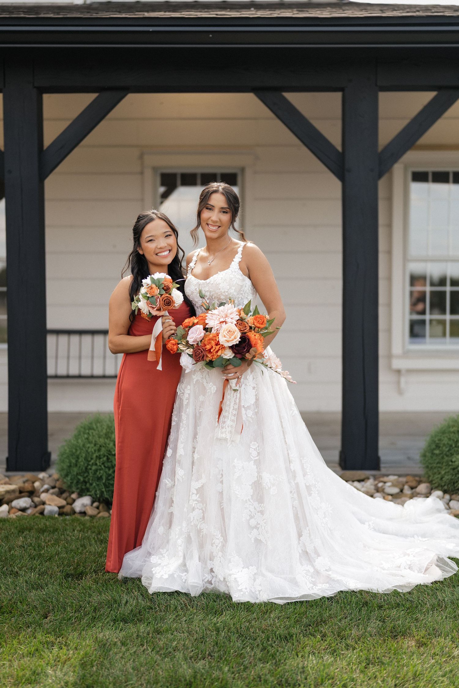 Wedding party members in coral dresses stand outdoors with the bride in a flowing white gown.