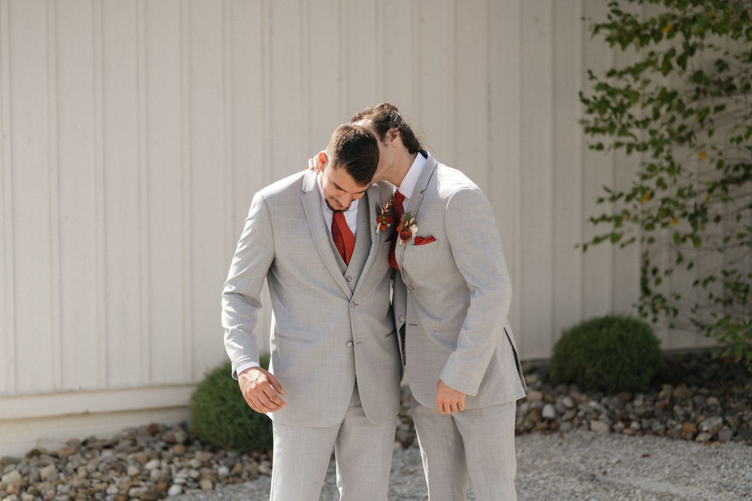 Groomsmen in matching light gray suits and red ties posing against white building exterior.
