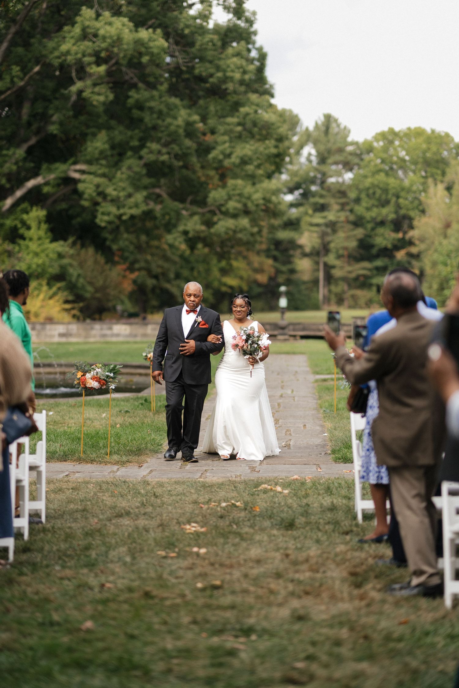 Outdoor wedding ceremony setup with white chairs lining a natural path through grassy grounds.