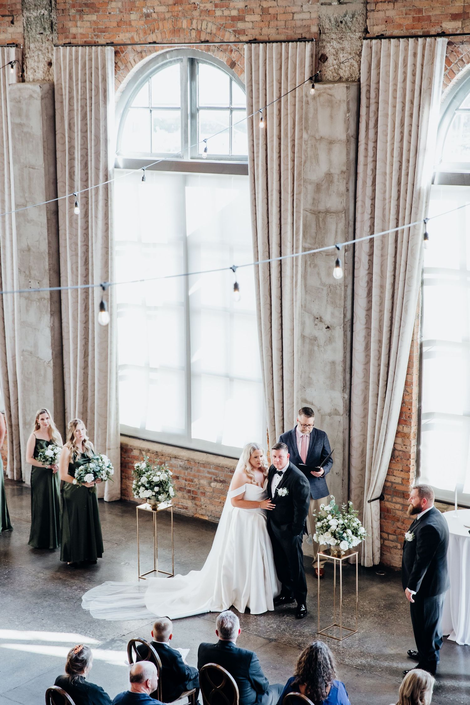 Wedding ceremony in an industrial chic venue with exposed brick walls and tall arched windows.