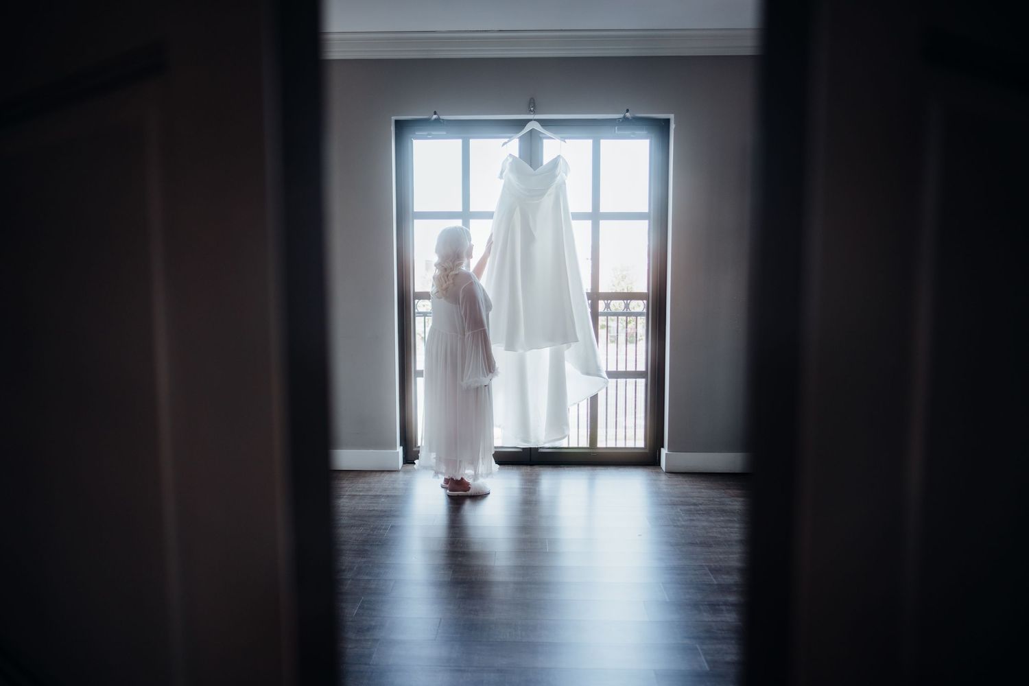 Silhouette of a person in a wedding dress standing in front of a bright window.