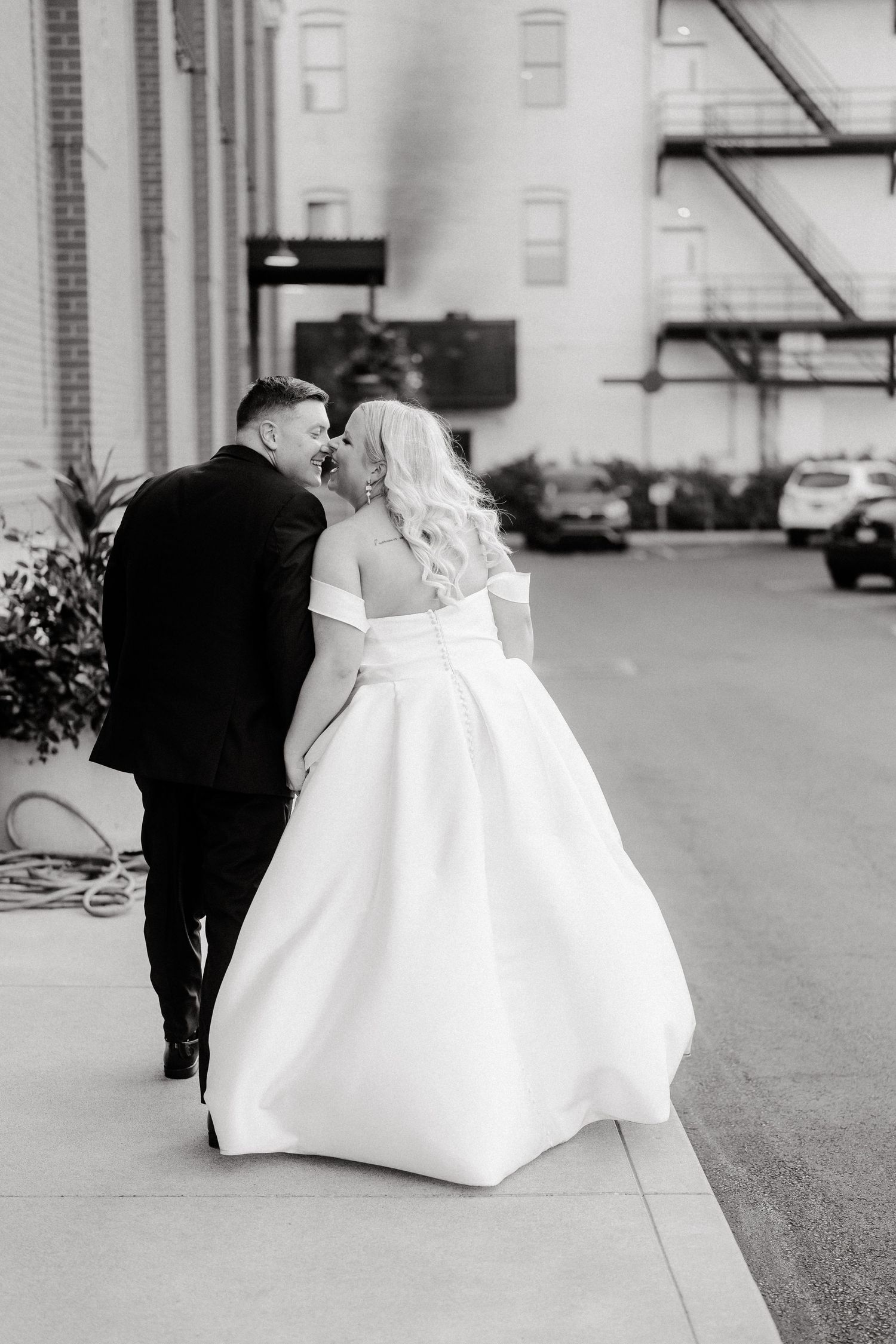 Black and white wedding photo capturing couple walking on urban sidewalk.