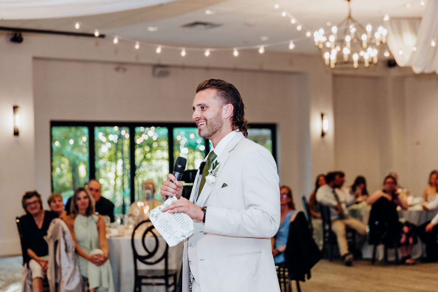 Modern wedding reception space decorated with elegant chandeliers and string lighting.