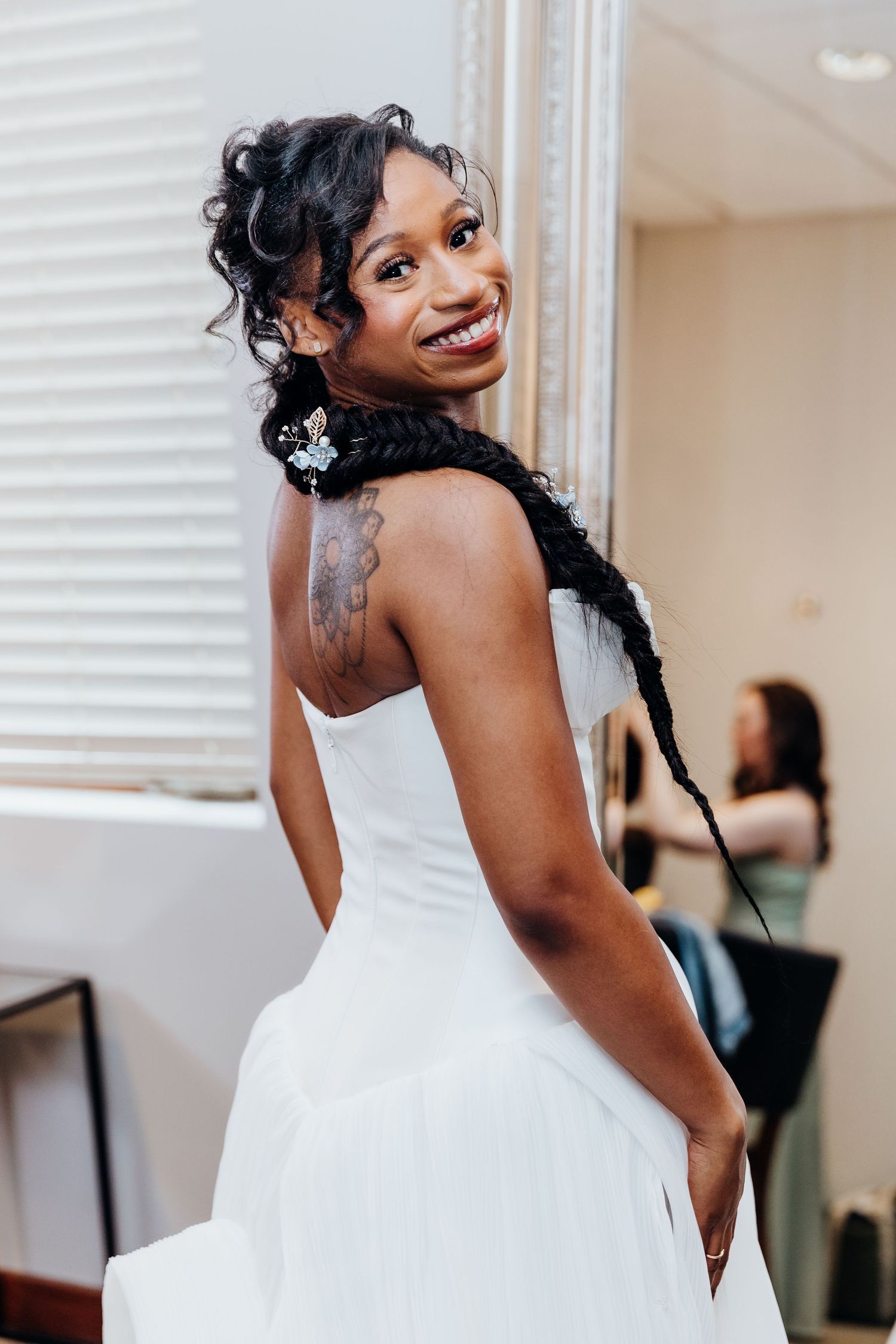 A person in a stunning white wedding dress smiles joyfully while posing in an indoor setting.