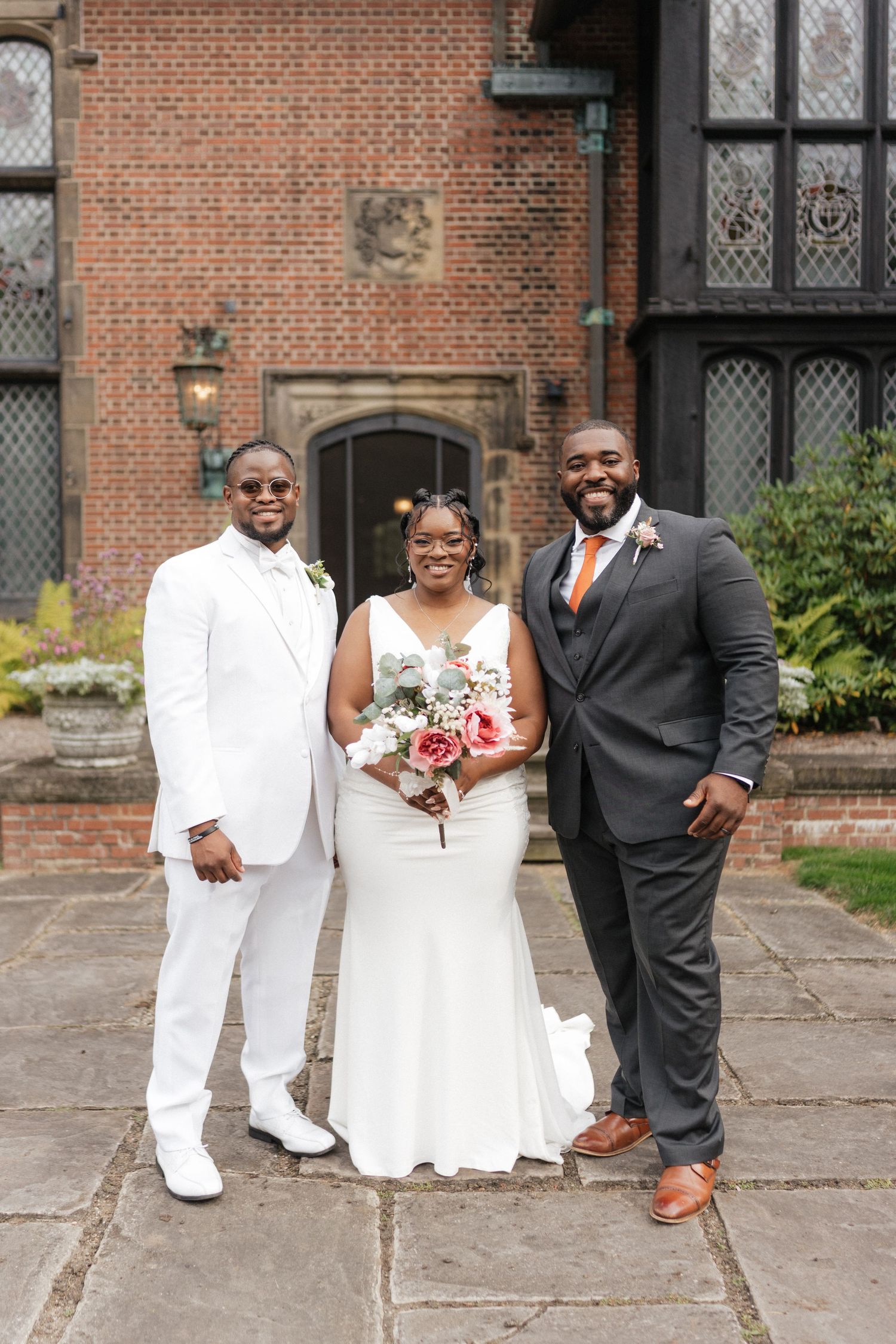 Wedding party poses together outside historic brick church building in coordinated white and black attire.