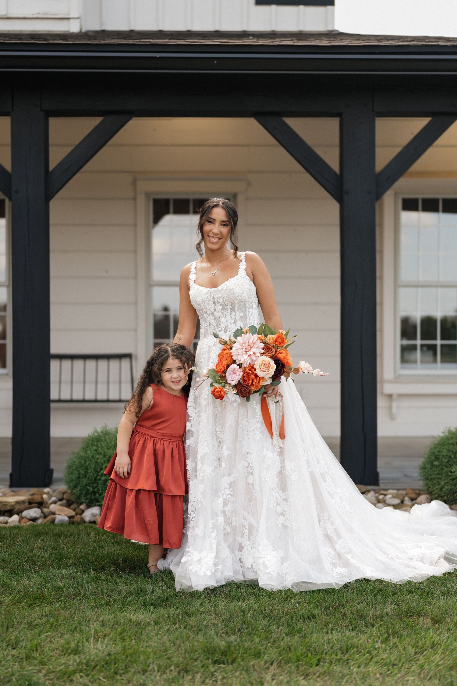 Wedding party members in orange and white dresses posing on porch of white building with black trim.