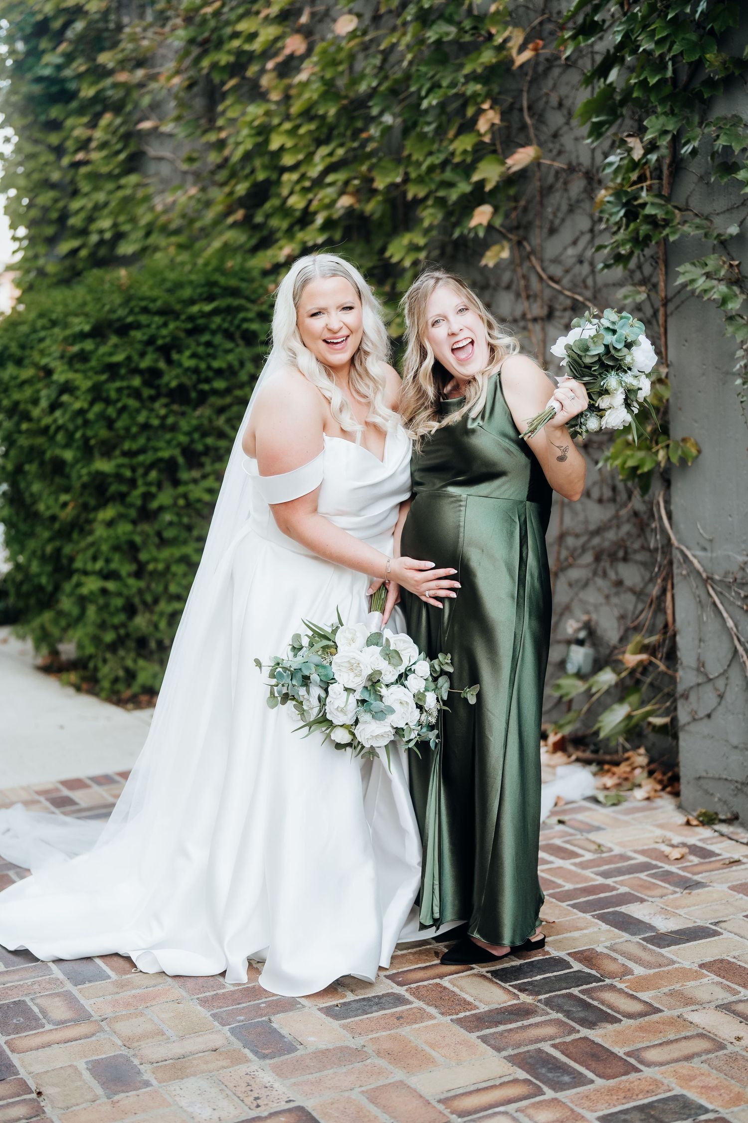 Wedding party members in white and sage green dresses pose together on brick pavement.
