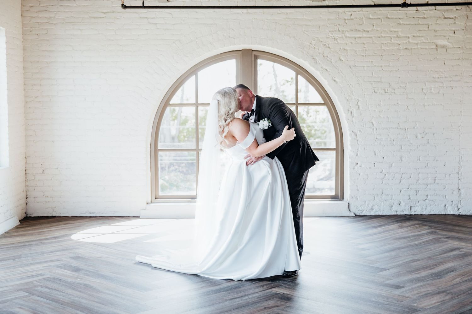 Elegant couple dances in a bright white room with arched windows and hardwood floors.
