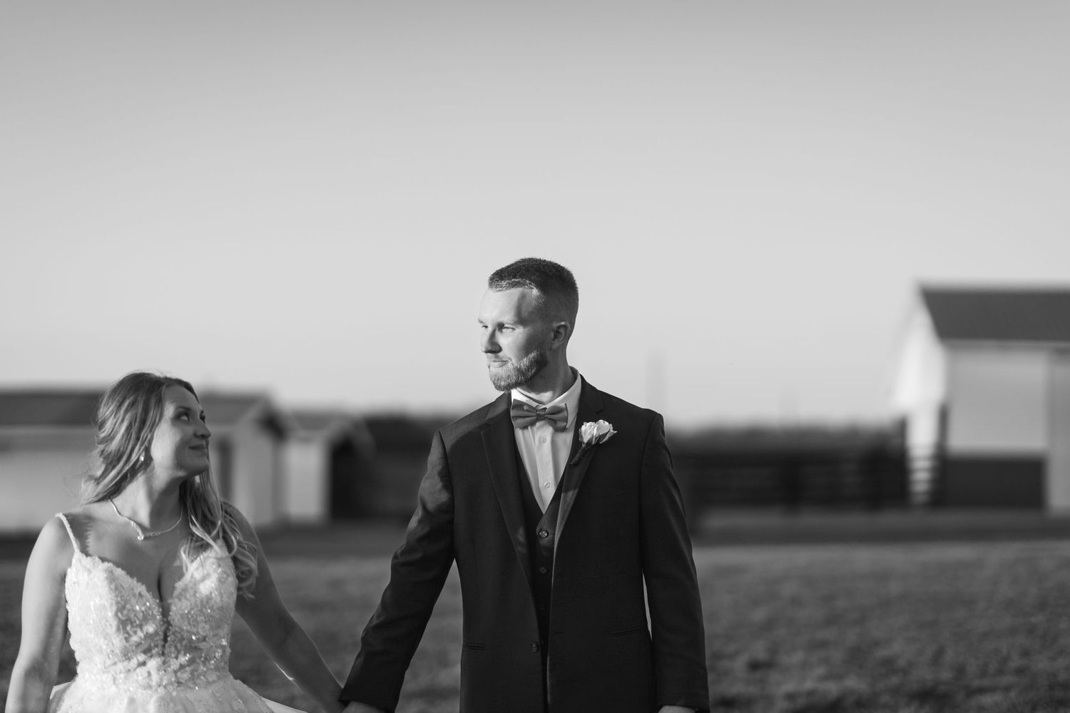 A black and white portrait of a wedding couple holding hands in an open field.