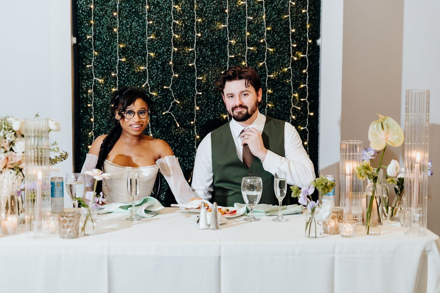 Wedding reception head table decorated with white linens and twinkle light backdrop.