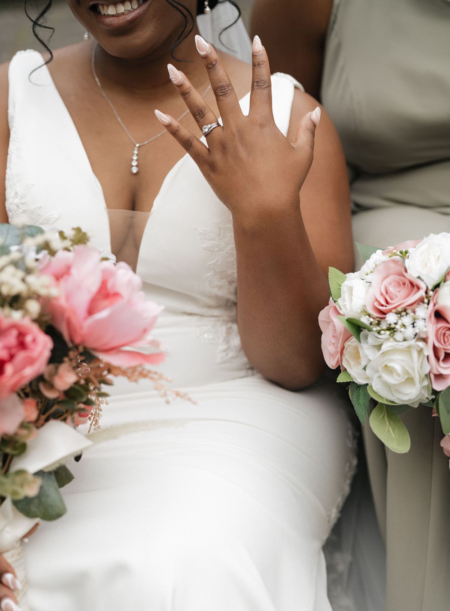 Close-up of bride's hand showing wedding ring with pink and white floral bouquet.