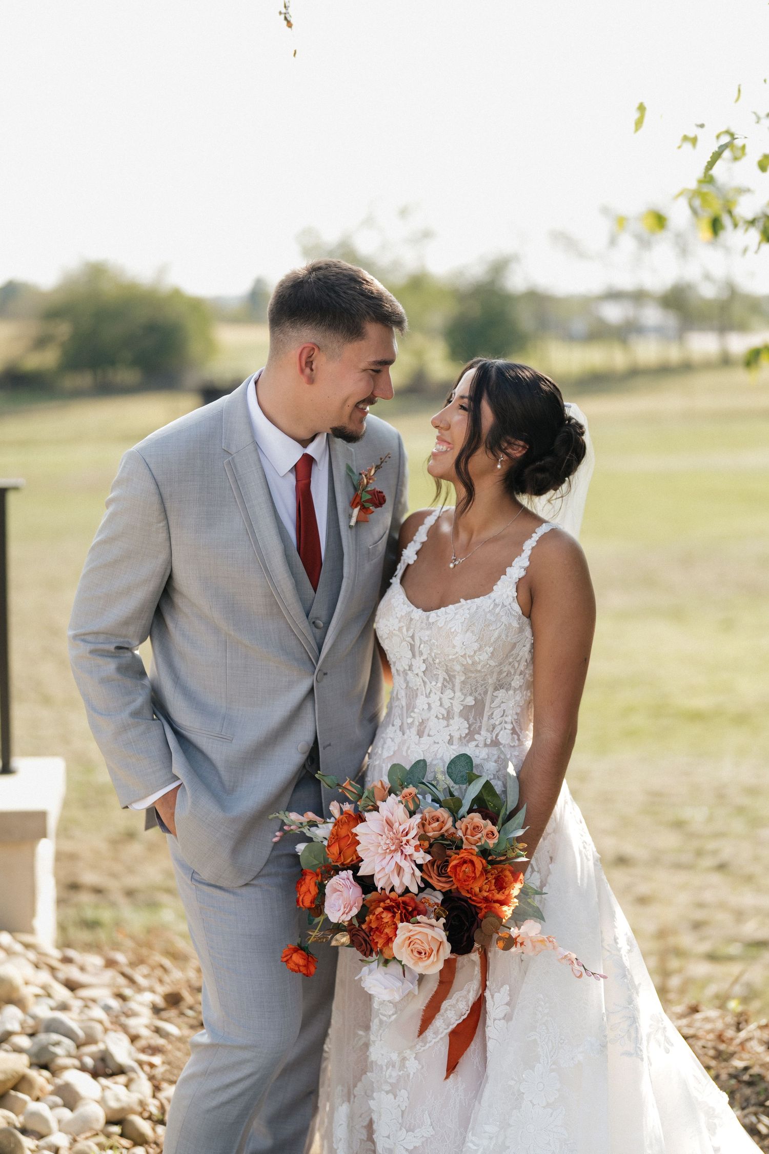 Romantic wedding portraits in a field with bride in lace dress and groom in light gray suit.