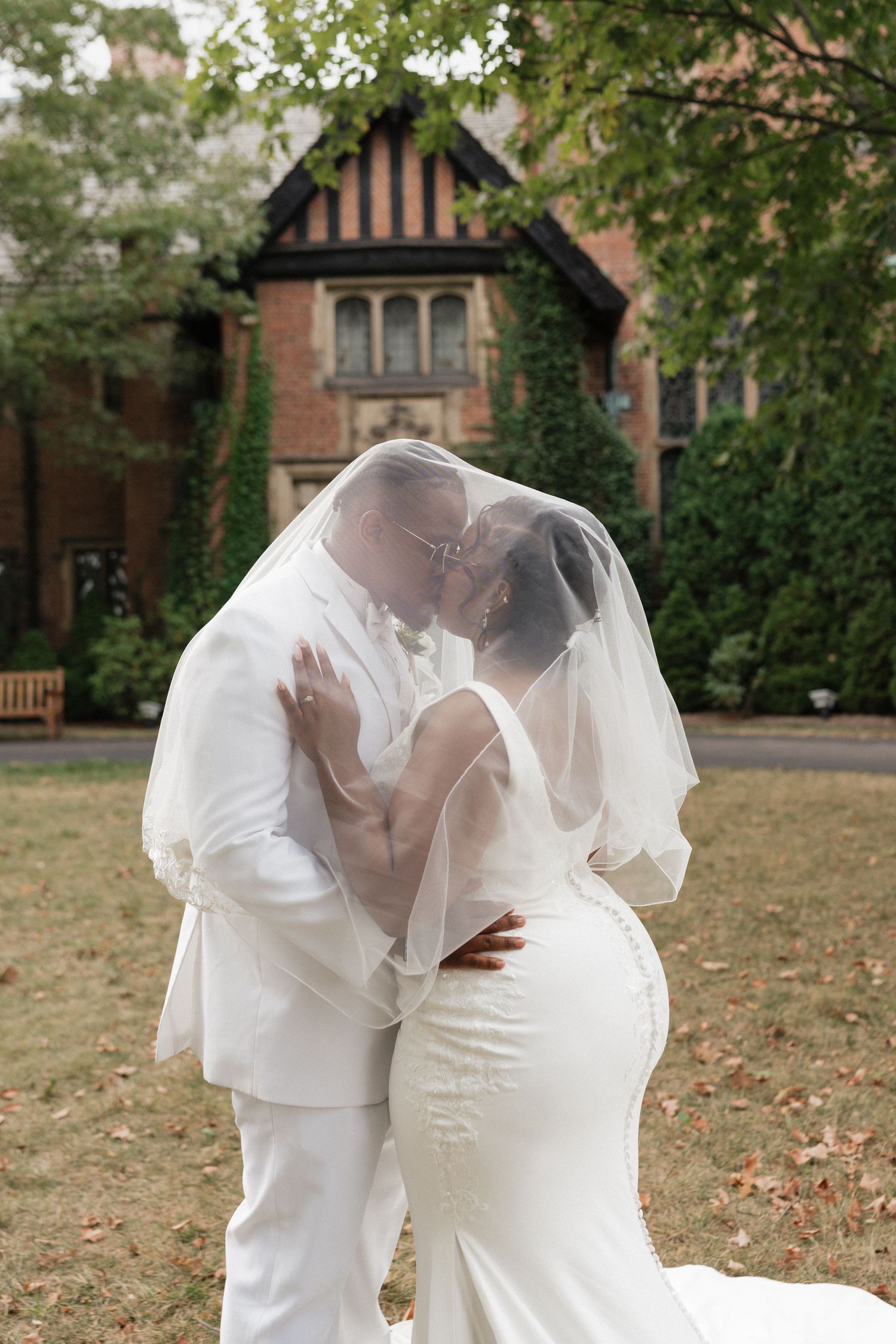 Newlyweds share an intimate moment under a flowing veil in front of historic architecture.