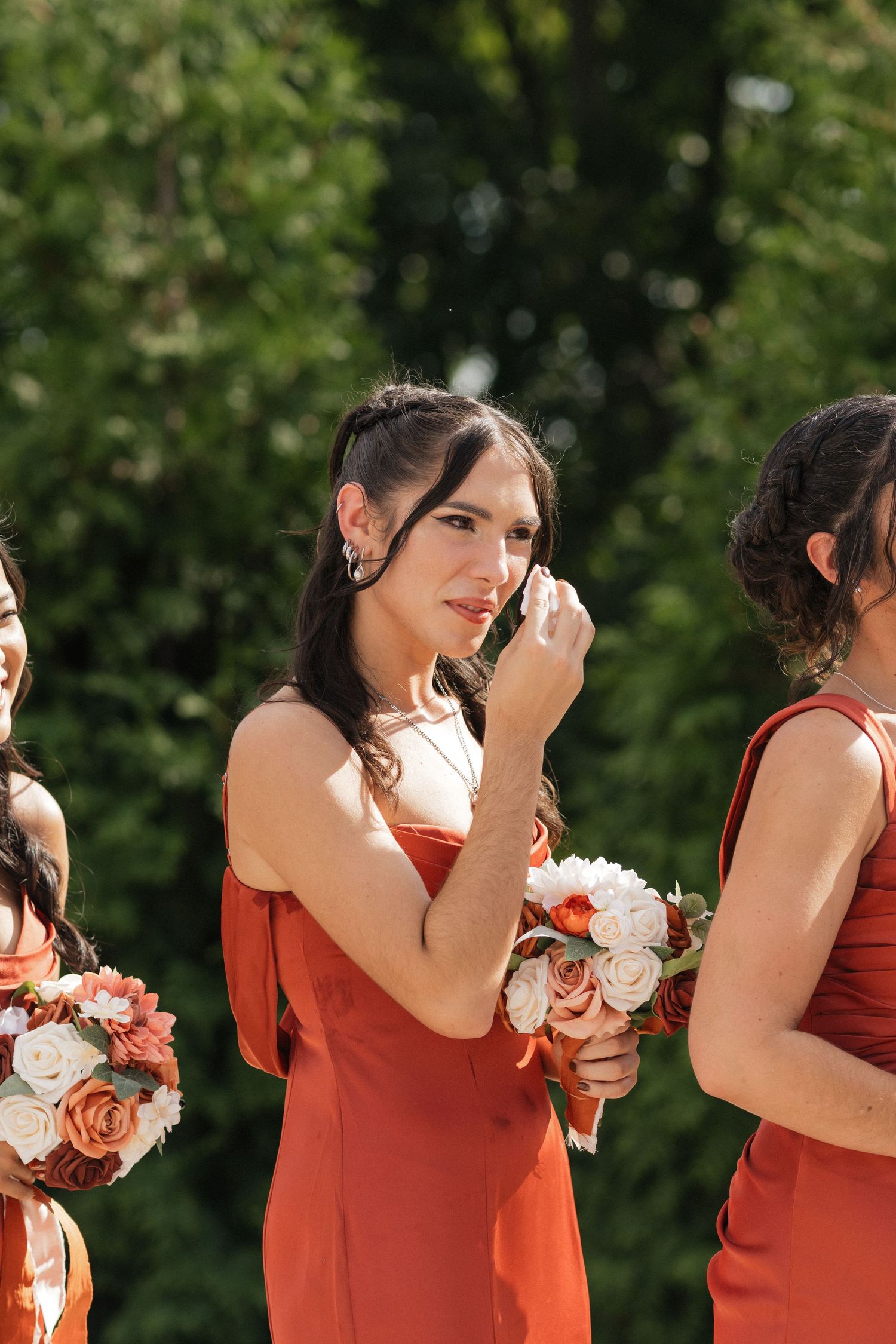 Bridesmaids in coral dresses holding bouquets during emotional ceremony moment.
