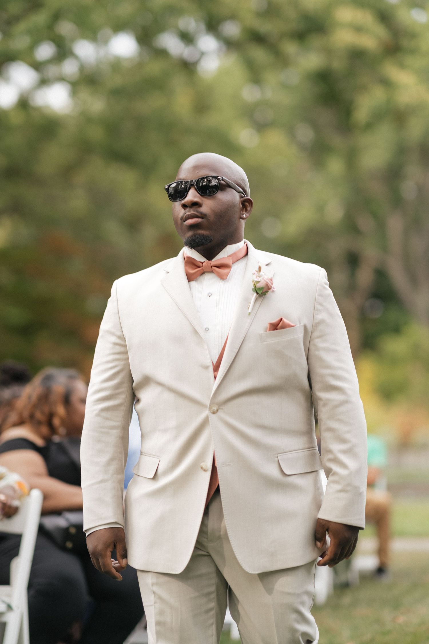 Wedding party members in cream-colored suits with coral bow ties stand in formation outdoors.