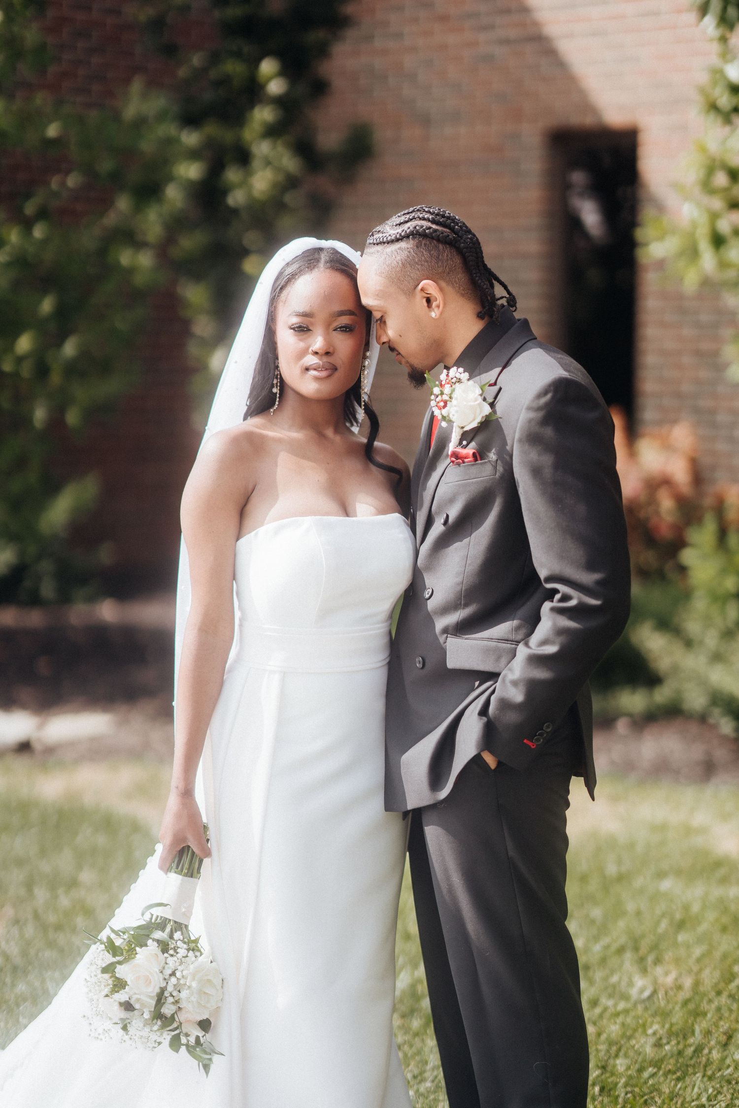 A romantic outdoor wedding portrait with a brick building backdrop and natural lighting.