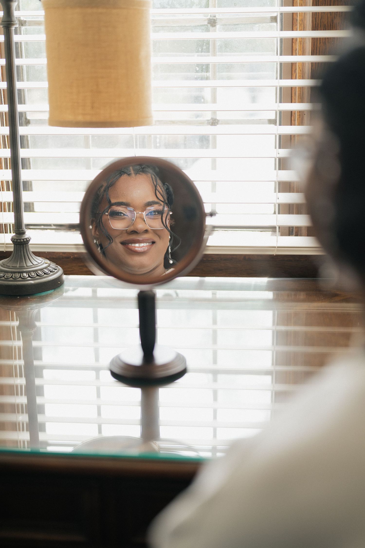 A reflection in a circular vanity mirror shows someone smiling while getting ready.