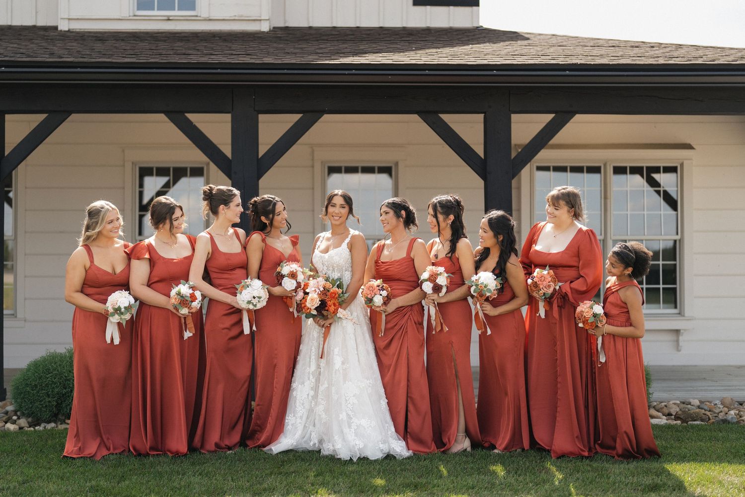 Wedding party poses outdoors in burgundy bridesmaids dresses and formal attire.